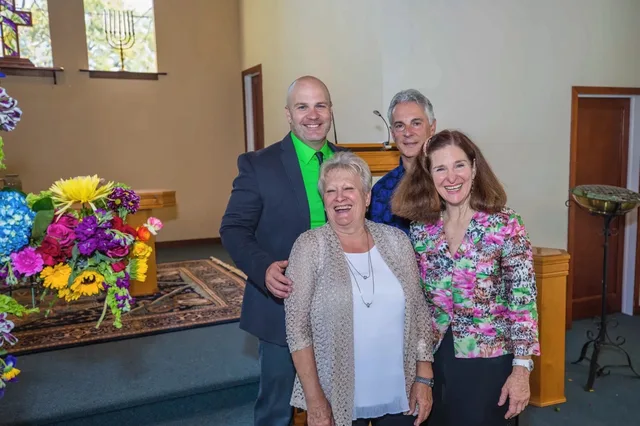 Four smiling church members near the front of the sanctuary beside a bouquet of flowers