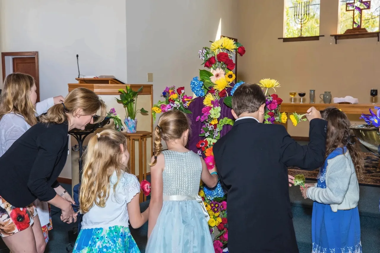 Children placing fresh flowers on the wooden cross at the front of the sanctuary